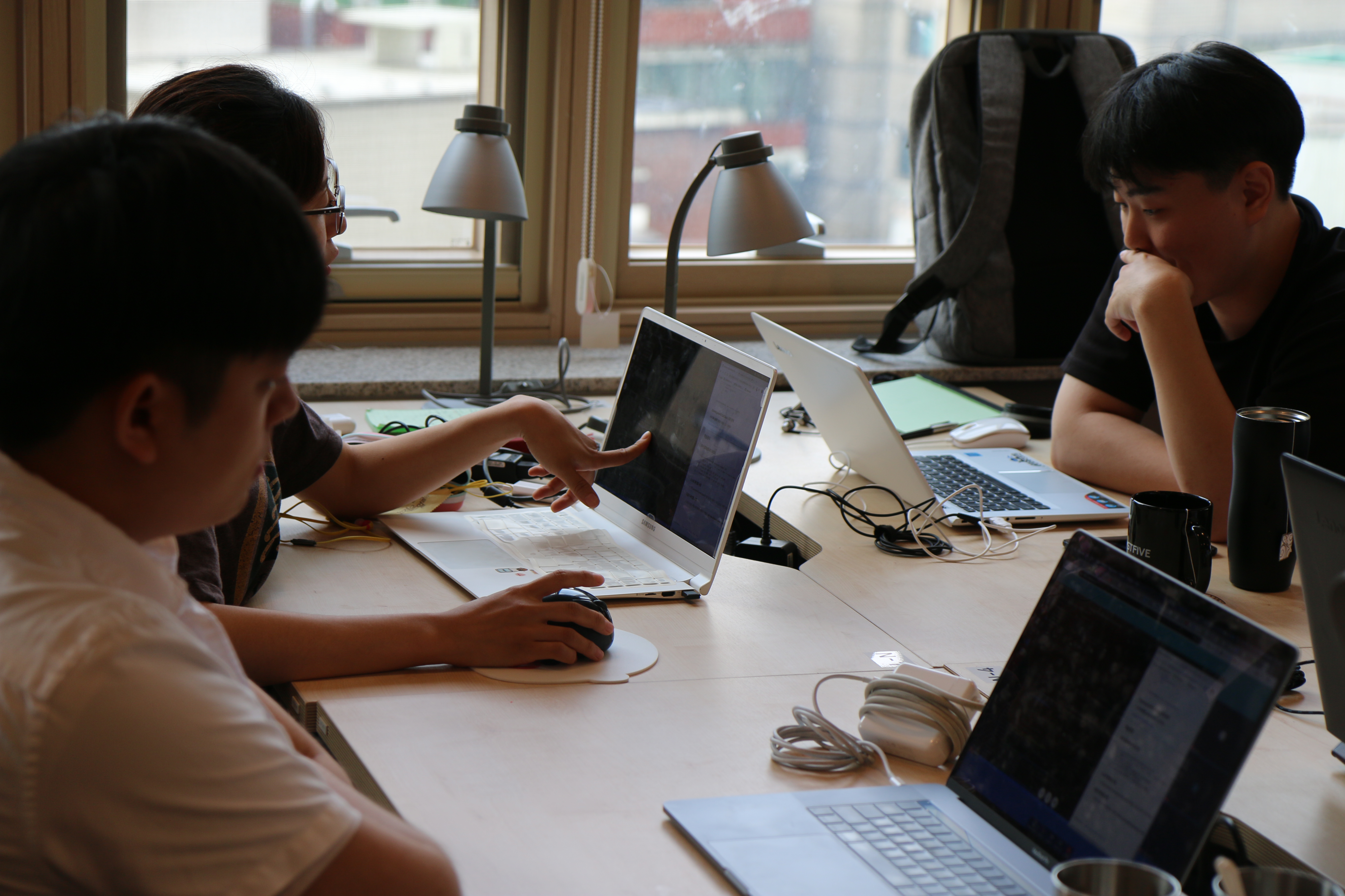 강의실에서 교육생들이 각자의 노트북을 앞에 두고 화면을 가리키며 서로 의견을 주고받는 모습입니다.