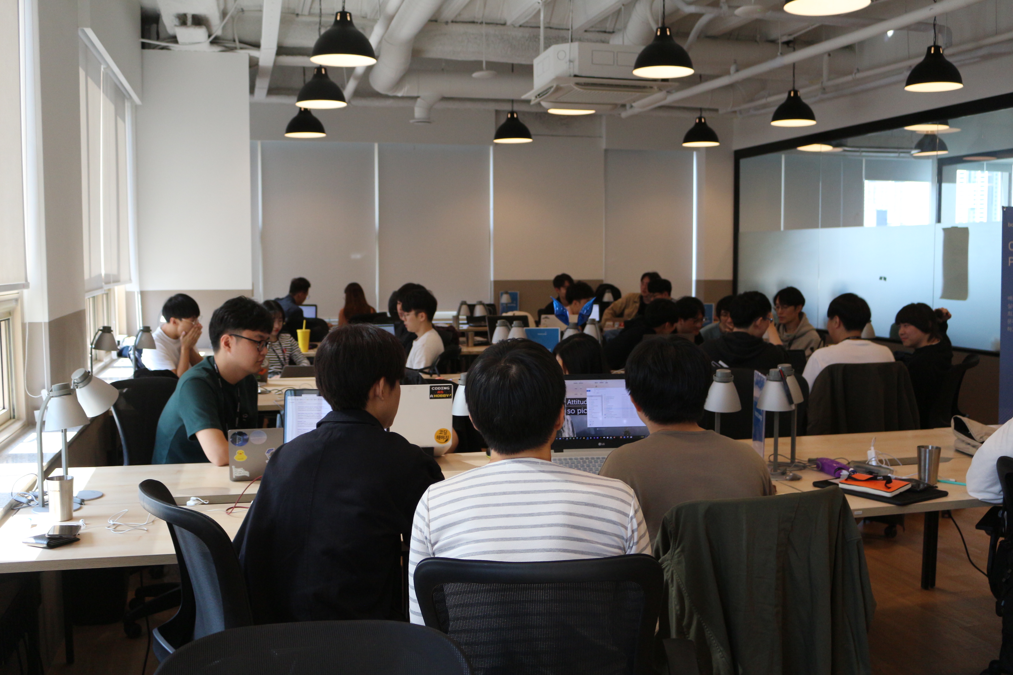 넓은 교육장에서 많은 교육생이 각자 노트북을 이용해 학습에 몰입하거나 동료들과 자유롭게 소통하고 있는 전경 사진입니다.